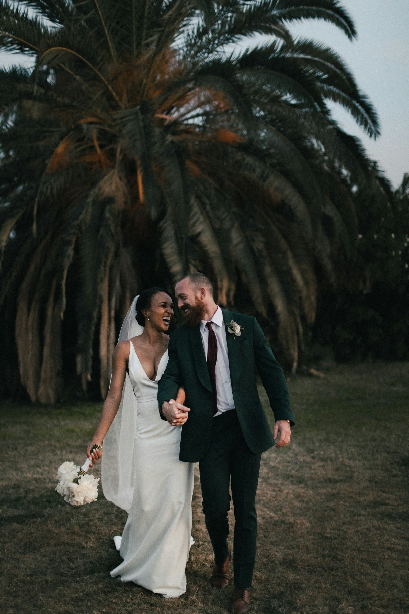 Couple laughing together under a palm tree at dusk