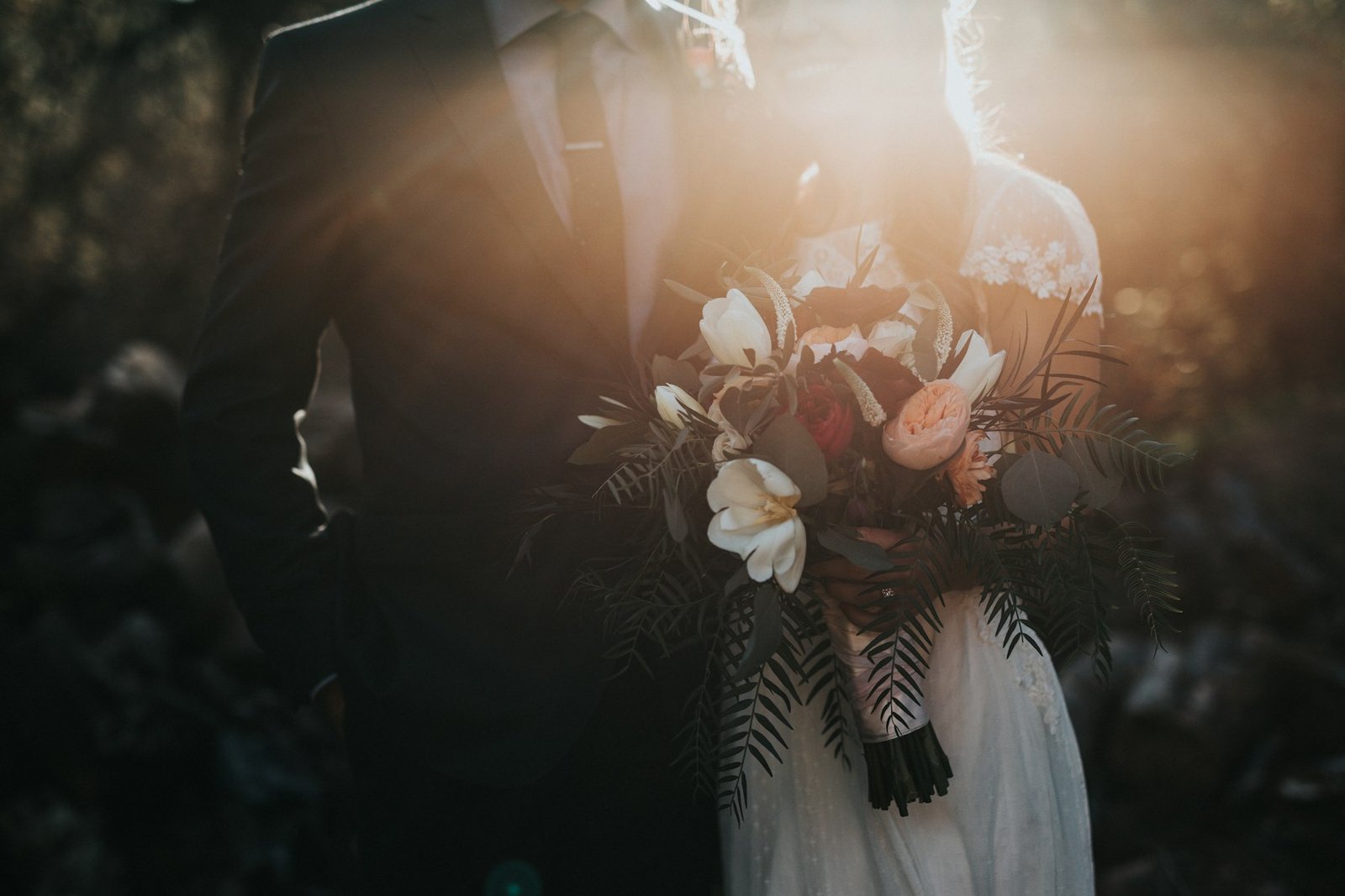 Backlit bridal bouquet of white and burgundy flowers at sunset